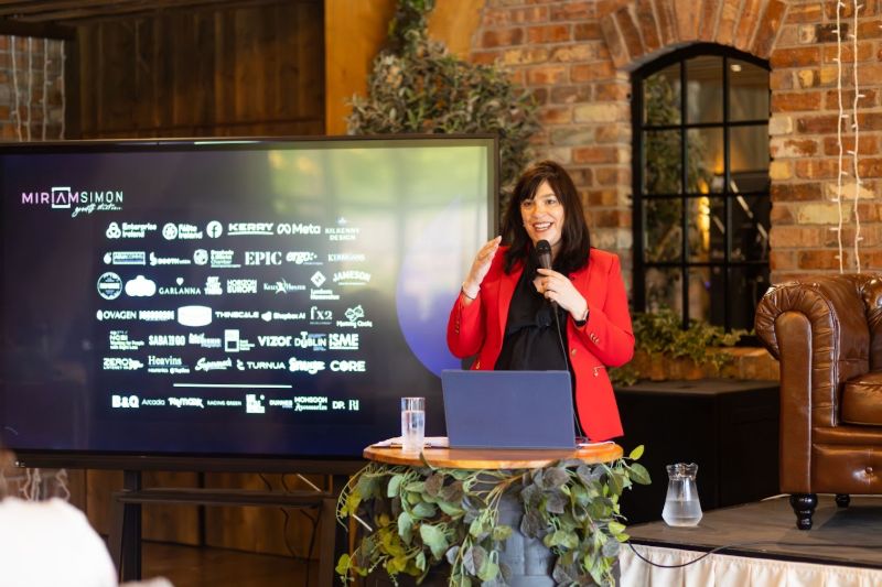 Miriam Simon speaking at Women in Business, Local Enterprise Office Leitrim, Longford and Westmeath, in front of her client-logo wall